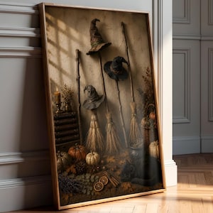 May include: A framed wall art print depicting three witch hats perched on wooden broomsticks, arranged against a textured wall. The scene includes stacked books, a lit candle, pumpkins, dried foliage, and a black cat resting on the floor.
