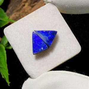 May include: Two triangular-shaped pieces of deep blue lapis lazuli gemstone with visible natural inclusions and a polished surface. The stones are arranged side-by-side to form a larger triangular shape, showcasing vibrant blue hues and dark flecks.