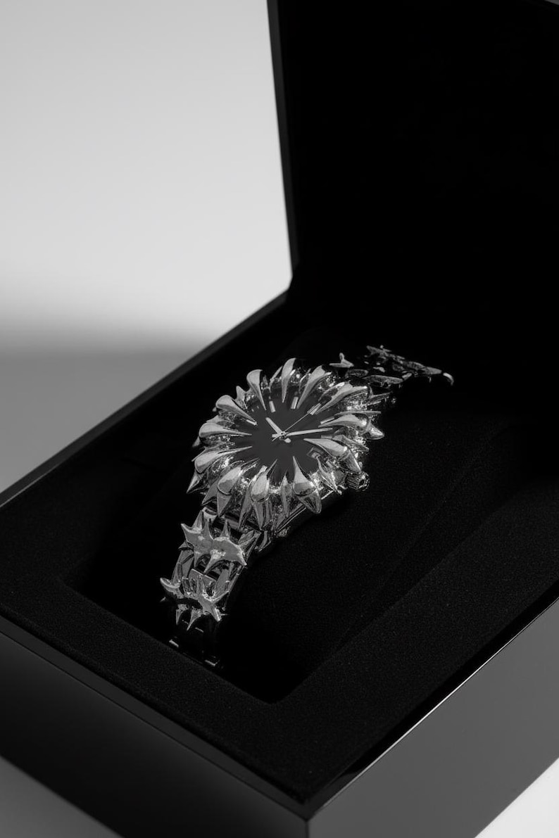 May include: A unique silver-toned wristwatch with a black face, presented in a black box. The watch features a spiky, starburst-like design around the face and on the band, creating a bold, avant-garde aesthetic.
