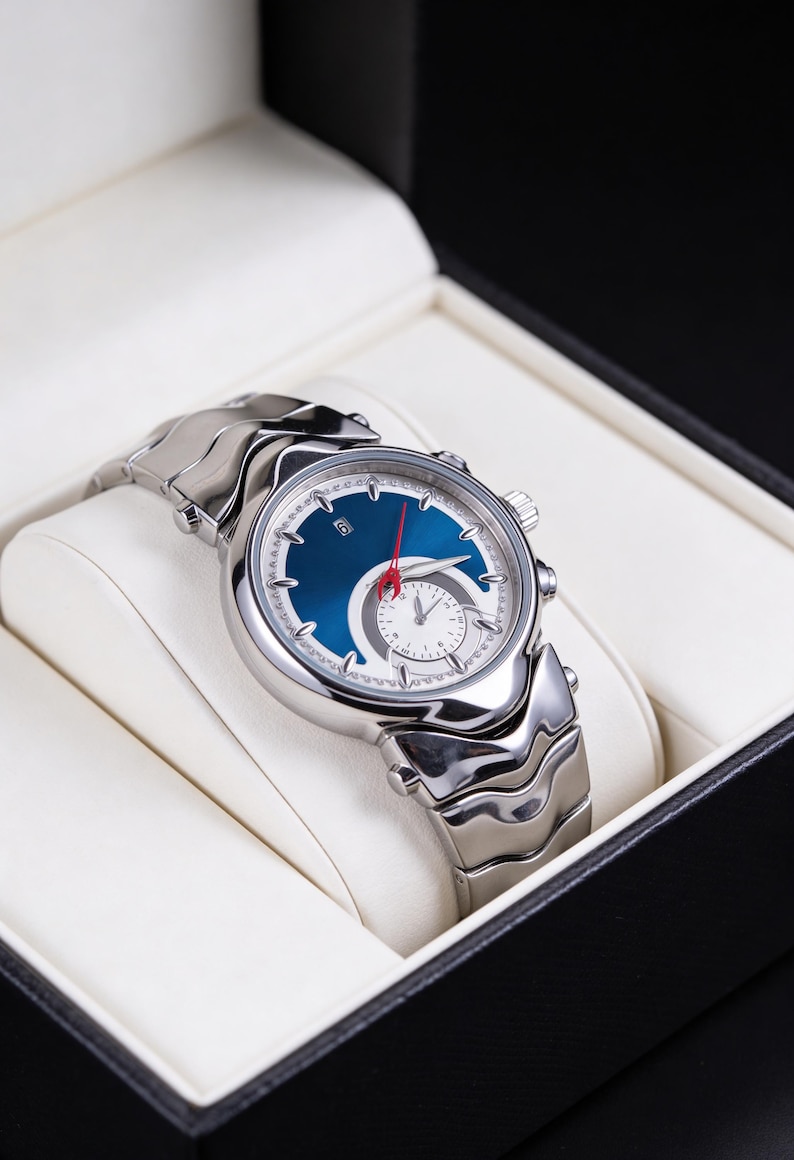 Pu&ograve; includere: Orologio da polso argentato con quadrante blu e lancetta dei secondi rossa, presentato in una scatola nera con interno bianco. L'orologio ha un design unico con un quadrante bianco pi&ugrave; piccolo e un cinturino argentato.