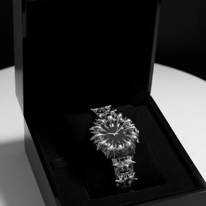 May include: A luxury wristwatch with a unique, spiky design, presented in a black box. The watch features a black face and a silver-toned, star-like bezel and band. The watch is displayed on a black velvet cushion.