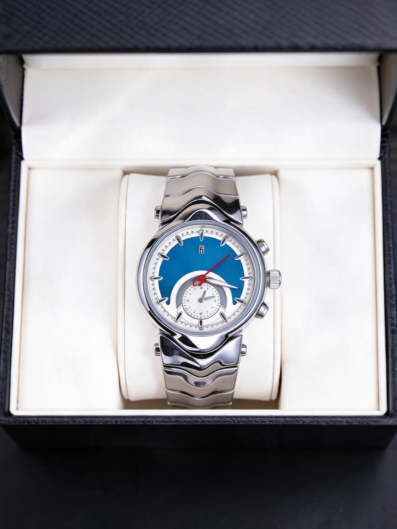Pu&ograve; includere: Un orologio da polso argentato con quadrante blu e cinturino argentato &egrave; presentato in una scatola nera con interno bianco. L'orologio ha un quadrante rotondo con lancette e indicatori argentati. Il cinturino &egrave; composto da maglie argentate.