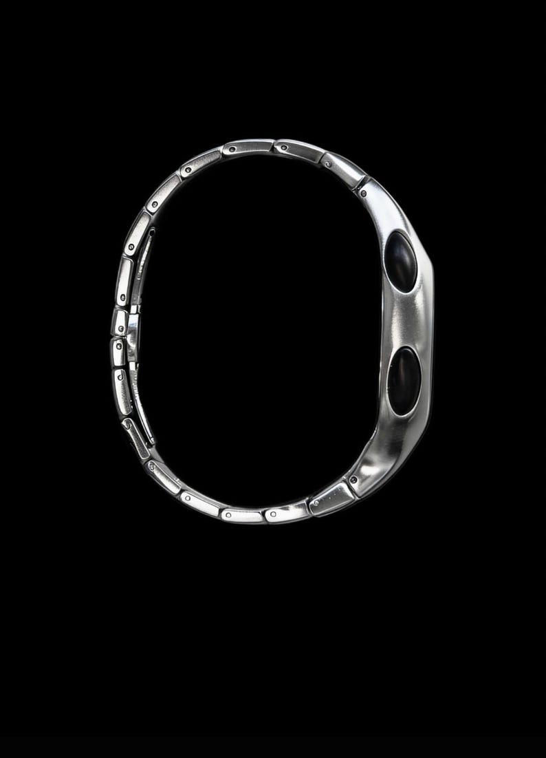 May include: A silver bracelet with a distinctive design. It features rectangular links leading to a curved, oval-shaped central element. The central element has two black, oval insets. The bracelet is set against a black background.