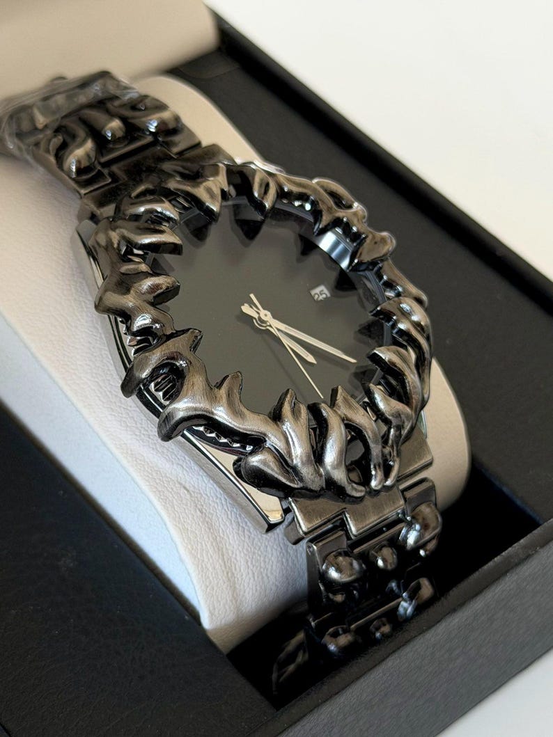 Puede incluir: Un reloj de pulsera negro con un bisel y una correa texturizados &uacute;nicos. La esfera del reloj es oscura con manecillas plateadas y una pantalla de fecha. El reloj se presenta en una caja negra con interior blanco.