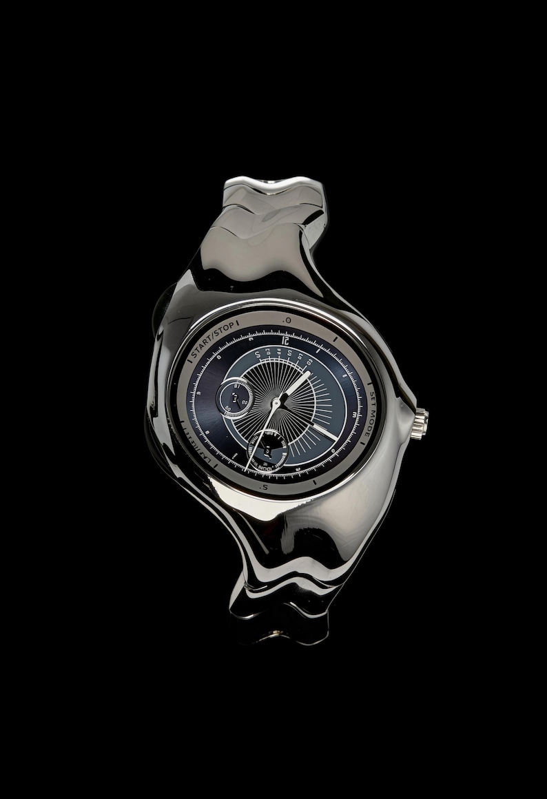 May include: A contemporary, silver wristwatch with a distinctive, fluid design. The watch face is dark with light grey accents and features multiple dials and hands. The text "START/STOP" and "SET MODE" are visible on the watch.