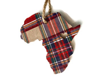 May include: A wooden ornament shaped like the continent of Africa, decorated with a red, green, and white plaid pattern. A small heart cutout is in the center of the ornament.
