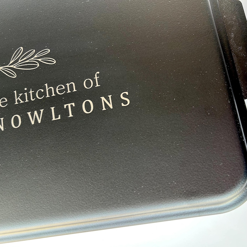 Może przedstawiać: Czarna forma do pieczenia z nadrukiem "The kitchen of the Nowltons" na przodzie.