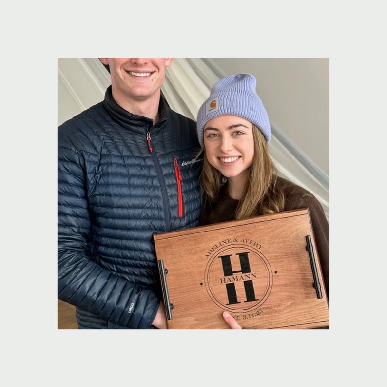 Young couple smiling holding a maple serving tray engraved with their names.