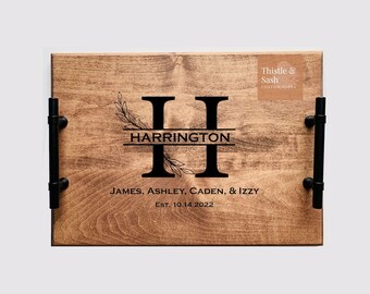 May include: A wooden serving tray with black metal handles. The tray is personalized with the letter "H", the name "HARRINGTON", the names "JAMES, ASHLEY, CADEN, & IZZY", and the date "EST. 10.14.2022".