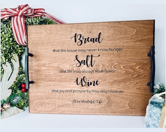 May include: A wooden serving tray with black metal handles. The tray has a quote from the movie "It's a Wonderful Life" inscribed on it: "Bread that this house may never know hunger. Salt that life may always have flavor. Wine that joy and prosperity may reign forever."