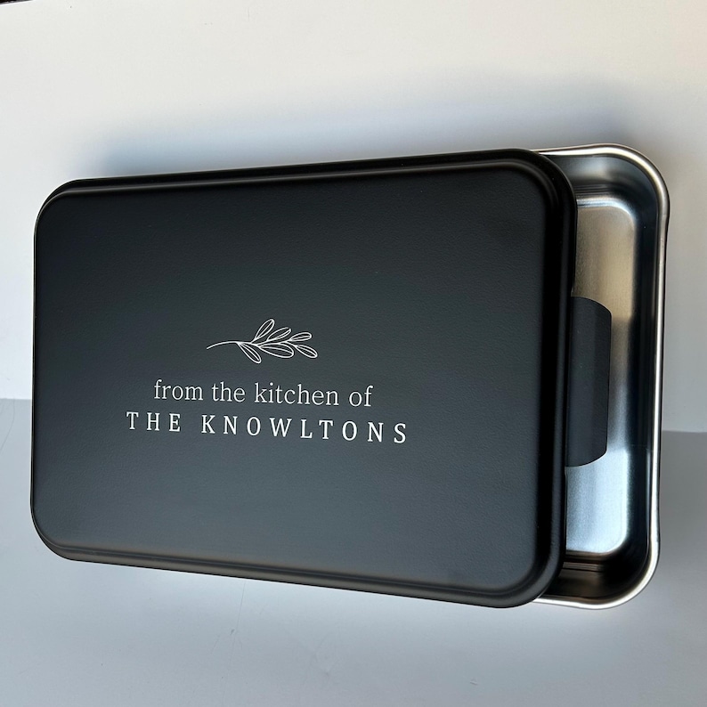 Może przedstawiać: Czarna forma do pieczenia z odpinanym pokrywką. Pokrywka ma biały wz&oacute;r z napisem "from the kitchen of THE KNOWLTONS" i małym wzorem gałązki.