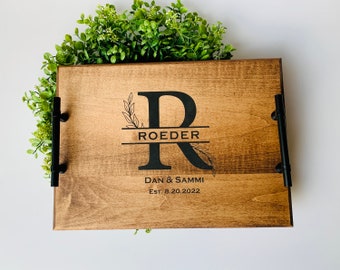 May include: A wooden serving tray with black metal handles. The tray is personalized with the last name "Roeder" and the initials "R" with a floral design. The text "Dan & Sammi Est. 8.20.2022" is also engraved on the tray.