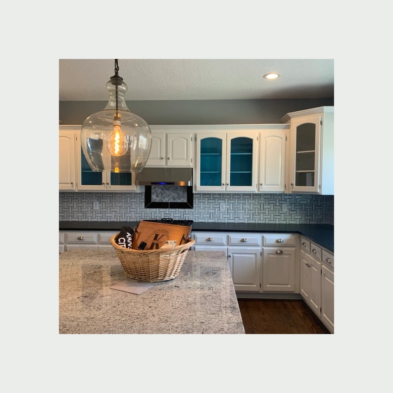 Large modern kitchen with white cabinets and granite countertops. Maple serving tray sitting in gift basket on countertop.