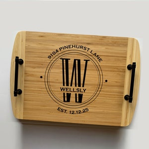 Two-toned bamboo serving tray. Circle monogram engraved in center, large W in the middle and the name Wellsly across. The 9104 Pinehurst Lane is curved at the top of the circle and the date at the bottom. Text and handles are black.