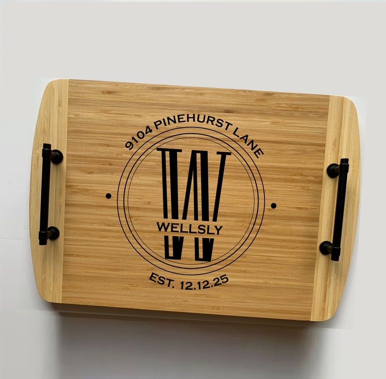 Two-toned bamboo serving tray. Circle monogram engraved in center, large W in the middle and the name Wellsly across. The 9104 Pinehurst Lane is curved at the top of the circle and the date at the bottom. Text and handles are black.