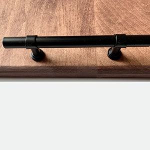 Close up of wooden serving tray edge, wood grain, and black steel handle.