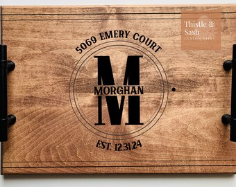 May include: A wooden serving tray with black metal handles. The tray is personalized with a black circle containing the letter "M", the name "MORGHAN", and the number "IV". The text "5069 EMERY COURT EST. 12.31.24" is also engraved on the tray.