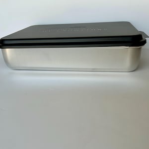 Może przedstawiać: Srebrna forma do pieczenia z czarną pokrywką. Pokrywka ma nadrukowane słowa "Nordic Ware".