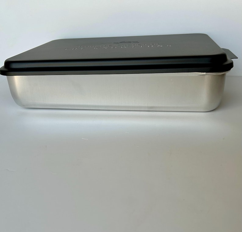 Może przedstawiać: Srebrna forma do pieczenia z czarną pokrywką. Pokrywka ma nadrukowane słowa "Nordic Ware".