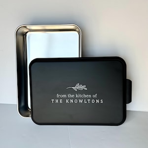 Może przedstawiać: Czarna blacha do pieczenia z srebrną formą do pieczenia na g&oacute;rze. Blacha do pieczenia ma biały wz&oacute;r z napisem "from the kitchen of THE KNOWLTONS" z małym wzorem gałązki.