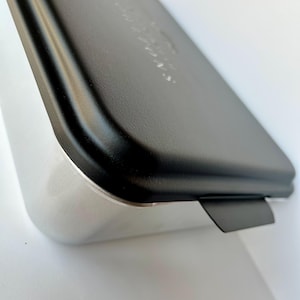 Może przedstawiać: Srebrna forma do pieczenia z czarną pokrywką. Pokrywka ma małą zakładkę, kt&oacute;ra ułatwia otwieranie.