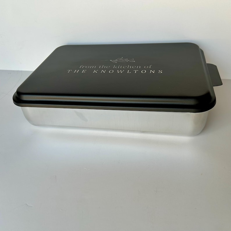 Może przedstawiać: Czarna metalowa forma do pieczenia z srebrnym wnętrzem i pokrywką. Na pokrywce znajduje się napis "From the kitchen of THE KNOWLTONS".