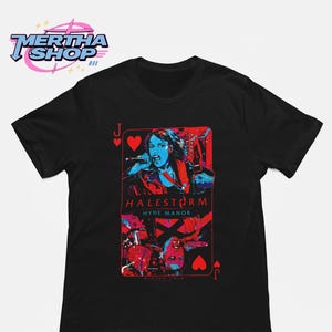 May include: A black short-sleeve t-shirt featuring a graphic of a playing card with a Jack of Hearts design. The print displays a person singing into a microphone with the text HALESTORM and HYDE MANOR in red and blue tones on a black background.