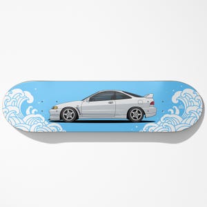 May include: A skateboard featuring a white sports car illustration set against a light blue background with stylized white waves. The car has black wheels and a spoiler. The board's design is reminiscent of Japanese art.