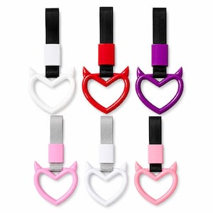 May include: Six heart-shaped car accessories in white, red, purple, and pink. Each has devil horn accents and a black or silver strap. Designed to attach to a car's interior.