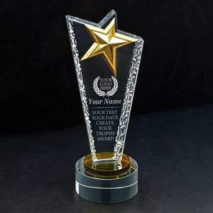 May include: A clear glass trophy featuring a gold star at the top and a circular base. The trophy includes etched text that reads: YOUR LOGO HERE, Your Name, YOUR TEXT, YOUR DATE, CREATE YOUR TROPHY AWARD. The edges have a textured, frosted finish.