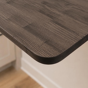 May include: A dark gray wooden tabletop with a visible wood grain pattern and a smooth, rounded corner edge. The surface features a rectangular plank construction with distinct joints where the individual wood pieces meet to form the flat top.