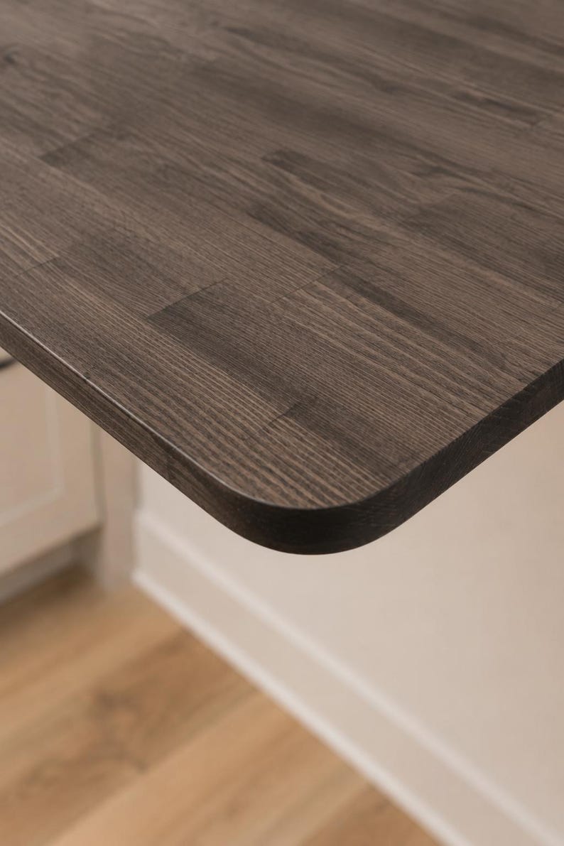 May include: A dark gray wooden tabletop with a visible wood grain pattern and a smooth, rounded corner edge. The surface features a rectangular plank construction with distinct joints where the individual wood pieces meet to form the flat top.