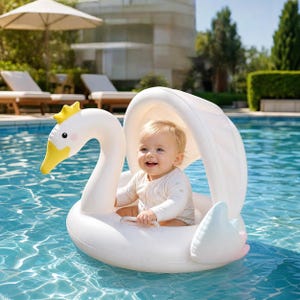 Op de afbeelding: Een opblaasbare witte zwaan zwemband voor baby's met een gele kroon en snavel, een gebogen nek en een geïntegreerde zonnekap. De zwemband heeft een ronde basis met een doorzichtig handvat om het kind veilig in het water te laten zitten.