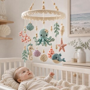 May include: A hanging nursery mobile featuring crocheted sea creatures including an octopus, seahorse, whale, starfish, and various shells in soft pastel colors. The items are suspended from a circular frame decorated with cream-colored trim.