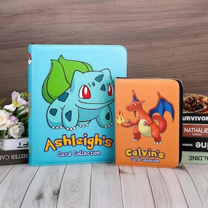 May include: A light blue card binder featuring a green Bulbasaur and the text Ashleigh's Card Collection, alongside a smaller orange card binder featuring a red Charizard and the text Calvin's Card Collection, both with black zippered edges.