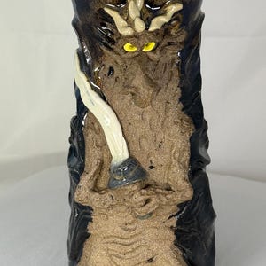 May include: A cylindrical ceramic mug featuring a sculpted, textured brown dragon figure holding a white sword. The dragon has bright yellow eyes and is set against a glossy, dark blue-black background. The text Dragon #01 Front View is visible.
