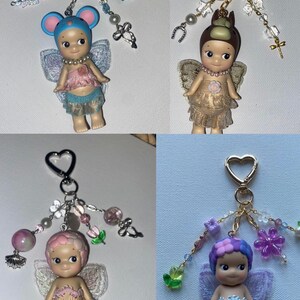 K&ouml;nnte beinhalten: Vier Schl&uuml;sselanh&auml;nger mit kleinen Engelfiguren mit Fl&uuml;geln, die jeweils mit dekorativen Perlen und Charms verziert sind. Die Figuren haben unterschiedlich gef&auml;rbte Haare und Outfits, mit Accessoires wie Schmetterlingen und Blumen.