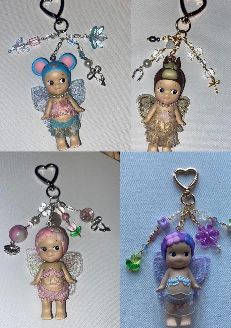 K&ouml;nnte beinhalten: Vier Schl&uuml;sselanh&auml;nger mit kleinen Engelfiguren mit Fl&uuml;geln, die jeweils mit dekorativen Perlen und Charms verziert sind. Die Figuren haben unterschiedlich gef&auml;rbte Haare und Outfits, mit Accessoires wie Schmetterlingen und Blumen.