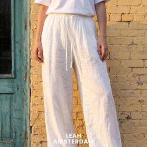 Peut inclure: Pantalon large blanc cass&eacute; dot&eacute; d'une taille &eacute;lastique avec un cordon de serrage assorti. Le pantalon est confectionn&eacute; dans un tissu textur&eacute; et est associ&eacute; &agrave; un t-shirt blanc uni. Le texte LEAH AMSTERDAM est visible en bas de l'image.