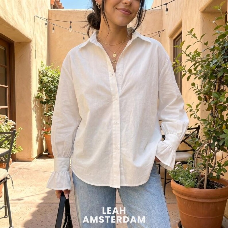 Puede incluir: Una camisa blanca de manga larga con botones, cuello cl&aacute;sico, tapeta frontal y pu&ntilde;os acampanados distintivos en las mu&ntilde;ecas. La prenda est&aacute; confeccionada con un corte estructurado y l&iacute;neas limpias en un tejido de color blanco s&oacute;lido.