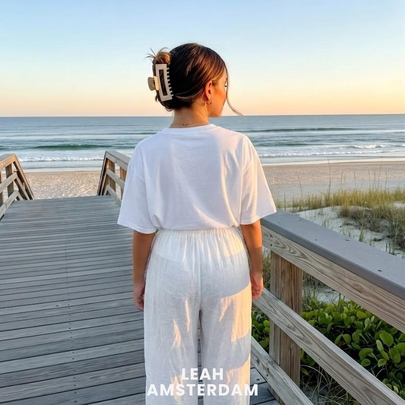 Peut inclure: Un t-shirt blanc uni &agrave; manches courtes et un pantalon blanc assorti. Les cheveux sont coiff&eacute;s en chignon, maintenus par une pince &agrave; cheveux rectangulaire beige. Le texte LEAH AMSTERDAM est imprim&eacute; en blanc au bas du centre de l'image.