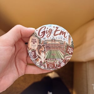 May include: A circular button featuring a graphic of Kyle Field, a collie dog, and a football. The text reads Gig 'Em, Texas A&M University, Kyle Field, Home of the 12th Man, Texas A&M, and Aggies. The design includes maroon and white colors.
