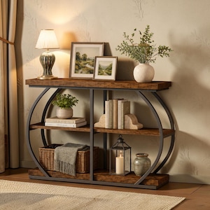 Könnte beinhalten: Eine rustikale Konsole mit einer dunklen Holzplatte und Regalen, getragen von einem schwarzen Metallrahmen. Der Tisch ist mit einer Lampe, gerahmten Landschaftsbildern, Büchern, einem Korb und einer Vase mit Grün dekoriert. Eine Kerzenlaterne und ein dekoratives Glas sind ebenfalls vorhanden.