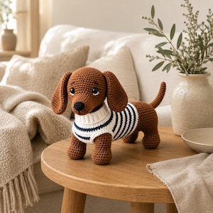May include: A brown crocheted dachshund toy wearing a white sweater with thin horizontal navy blue stripes. The dog has long floppy ears, a black nose, and dark eyes. The toy is standing on four short legs with a small tail pointing upward.