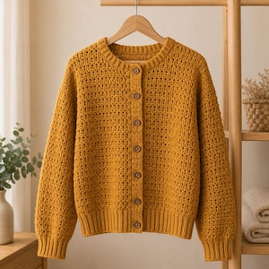 May include: A mustard yellow long-sleeve cardigan featuring a textured crochet knit pattern, a round neckline, and a front button closure with seven small brown buttons. The garment has ribbed cuffs and a ribbed hem, hanging on a wooden hanger.