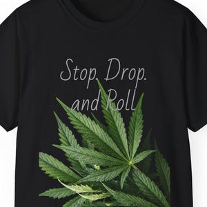 May include: Black t-shirt with a large green cannabis leaf design. The shirt has the text "Stop, Drop, and Roll" in a cursive font above the leaf. The shirt is a short-sleeved crew neck.