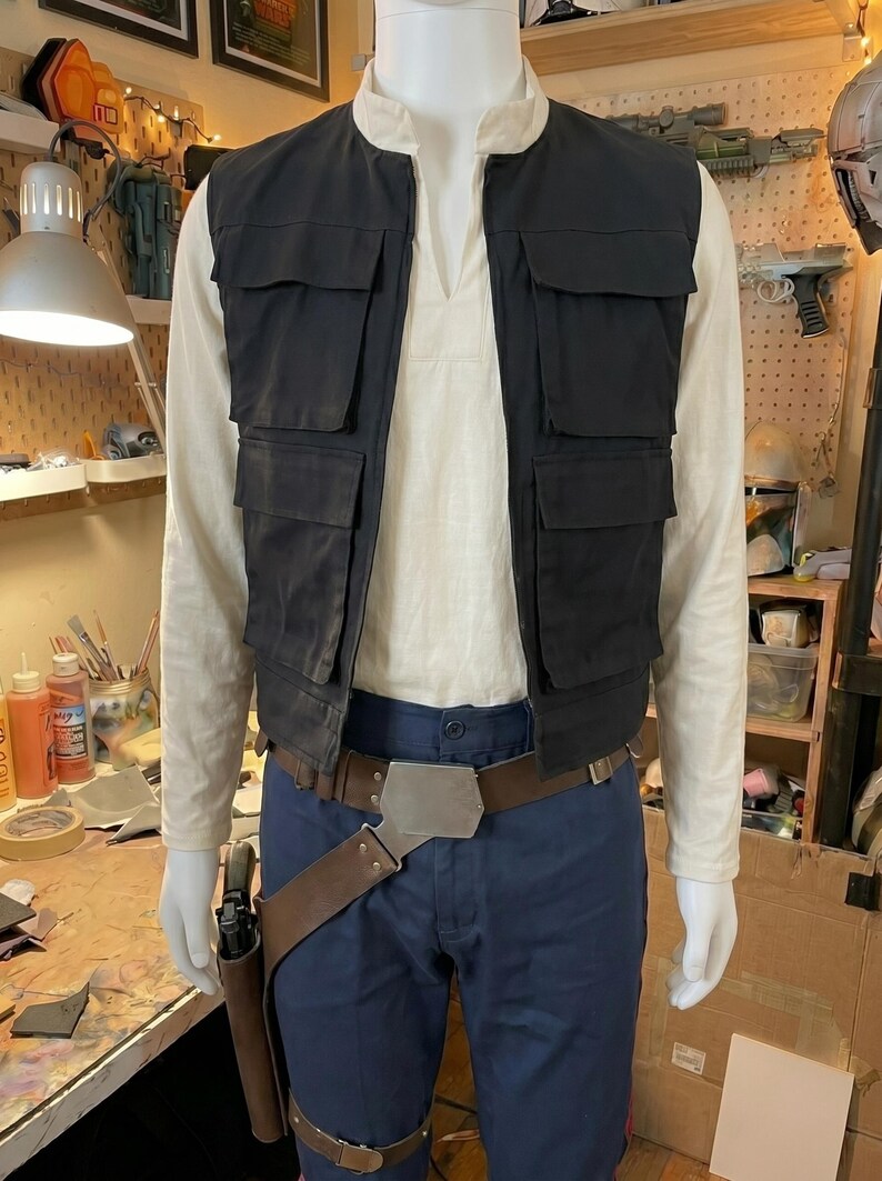 May include: A costume ensemble featuring a cream-colored long-sleeve shirt with a mandarin collar, a black utility vest with four front pockets, dark blue trousers, and a brown leather-style belt with a metal buckle and a side holster.