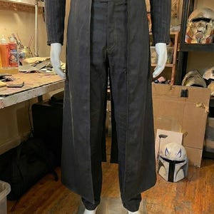 May include: A dark charcoal gray ensemble featuring a long, open-front overskirt layered over matching trousers. The top is a long-sleeved, pinstriped shirt. The overskirt has a structured waistband with a single button closure at the center front.