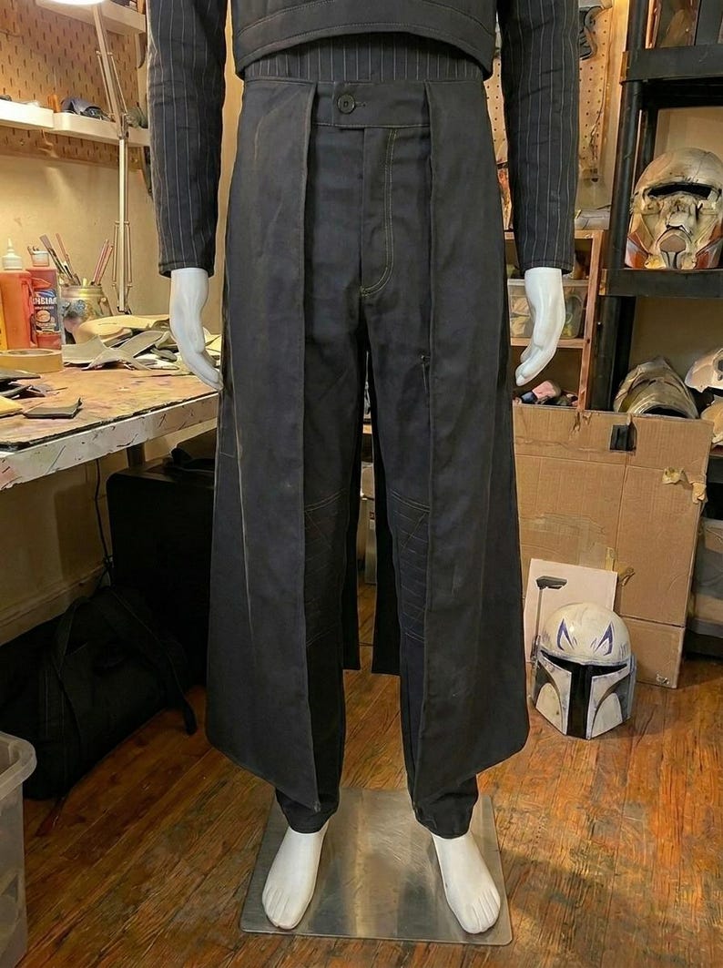 May include: A dark charcoal gray ensemble featuring a long, open-front overskirt layered over matching trousers. The top is a long-sleeved, pinstriped shirt. The overskirt has a structured waistband with a single button closure at the center front.