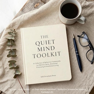 May include: A cream-coloured book titled The Quiet Mind Toolkit with black text, a dark blue fountain pen, black-rimmed glasses, a sprig of eucalyptus, and a white ceramic mug filled with black coffee, all arranged on a beige fabric surface.